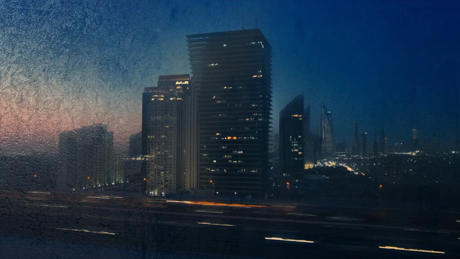 A city skyline at blue hour seen through a rain-streaked window
